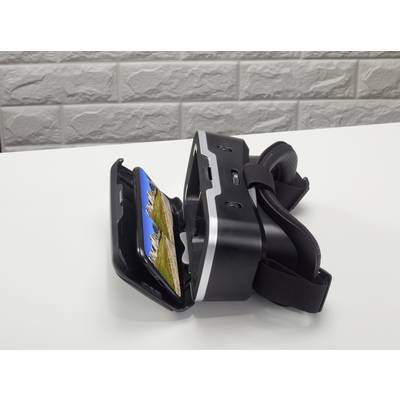 Virtual-Reality-Headset auf weißem Tisch, geöffnet mit einem Smartphone, das eine Berglandschaft anzeigt. Brickmauer im Hintergrund.