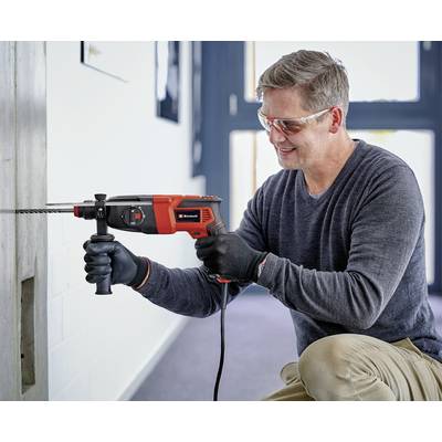 Ein Mann in Schutzbrille und Handschuhen bohrt mit einer elektrischen Bohrmaschine ein Loch in eine Betonwand.