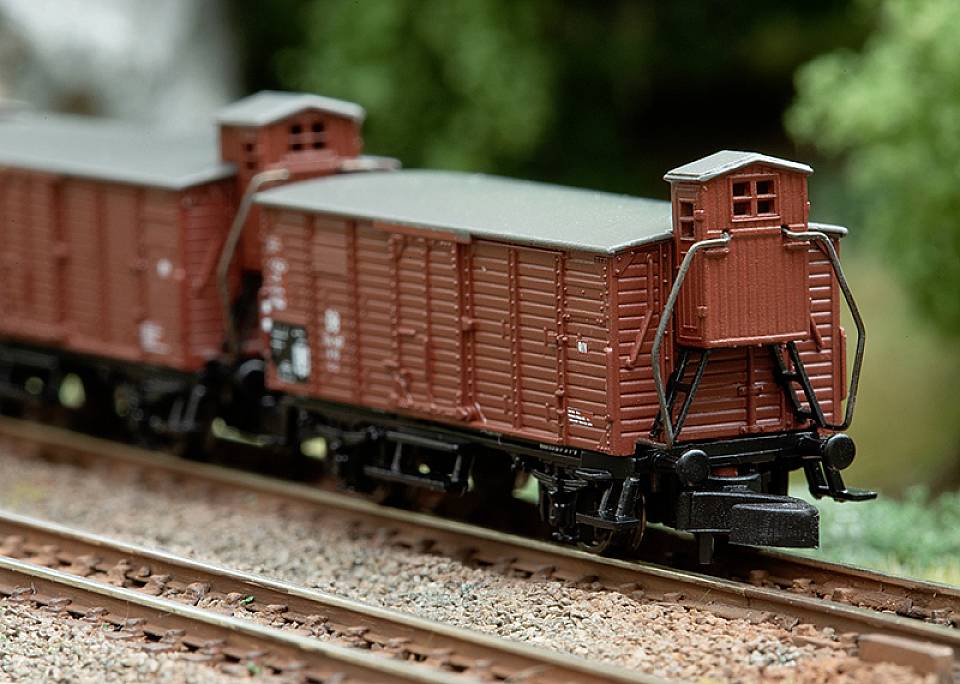 Modelleisenbahn mit zwei braunen Güterwaggons auf einem Gleis, umgeben von grüner Landschaft.