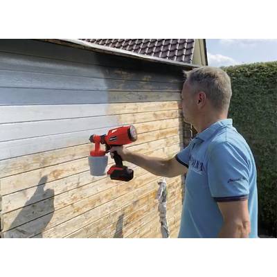 Mann sprüht dunkle Farbe mit einer Farbspritzpistole auf eine Holzwand; die Wand ist teilweise gestrichen.
