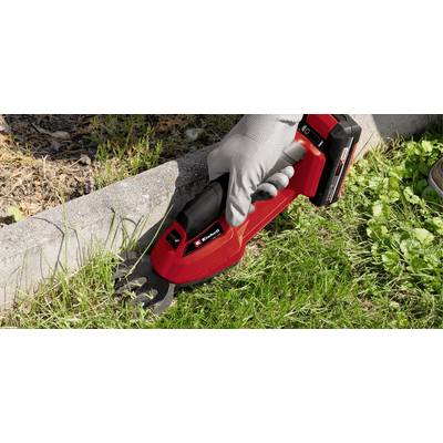 Eine Person schneidet mit einem roten Akku-Grasschneider Gras an einer Bordsteinkante.