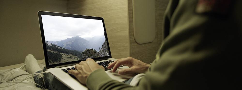 Eine Person tippt auf einem Laptop mit einem Berglandschaftsbild auf dem Bildschirm. Der Laptop befindet sich auf einem Tisch.