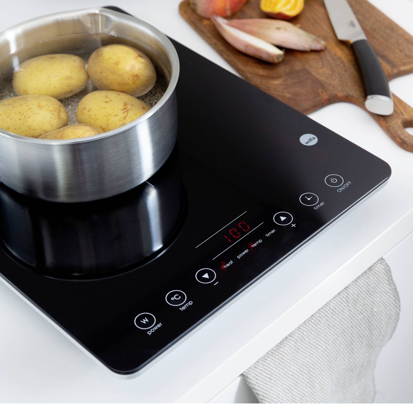 Ein Topf mit kochenden Kartoffeln steht auf einem schwarzen Induktionskochfeld. Daneben ein Holzbrett mit Zwiebeln und einem Messer.