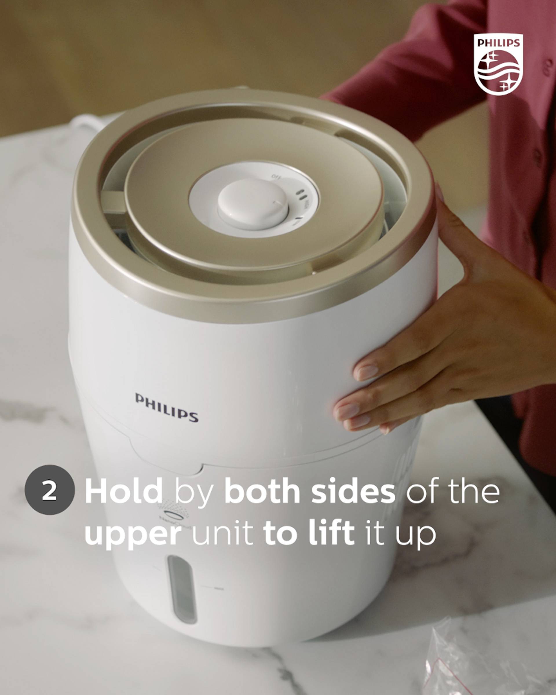 Person hält die obere Einheit eines Philips-Reinigers von beiden Seiten, um sie anzuheben. Anweisungen auf Englisch im Bild.