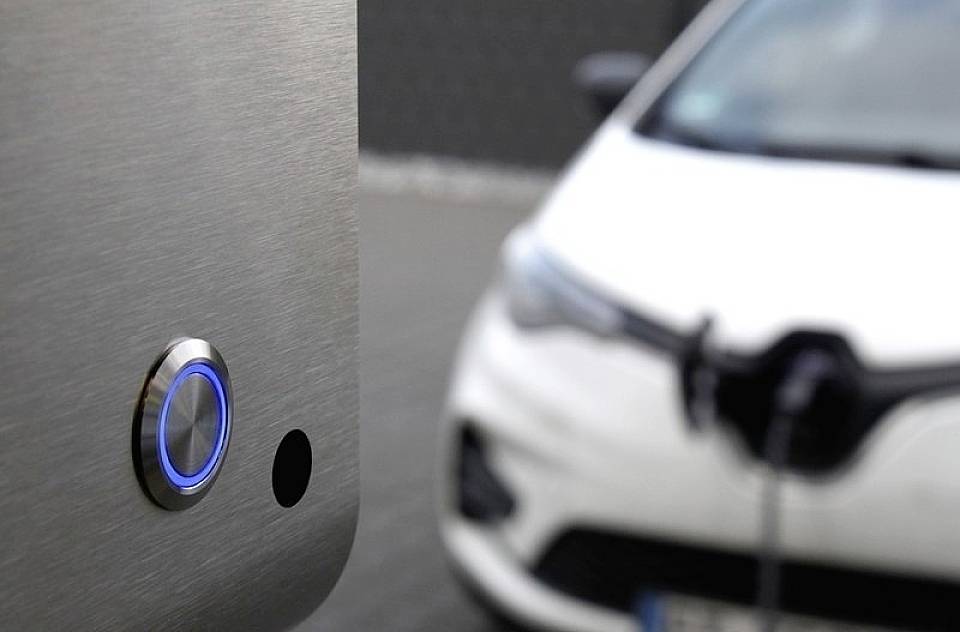 Ein Elektroauto ist zum Laden an eine Ladestation angeschlossen. Die Ladestation zeigt einen leuchtenden blauen Knopf.
