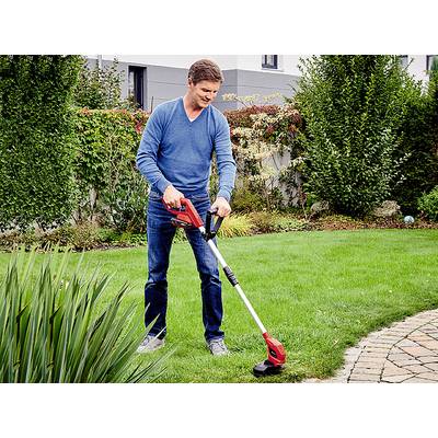 Ein Mann trimmt Rasen im Garten mit einem elektrischen Rasentrimmer neben einem gepflasterten Weg.