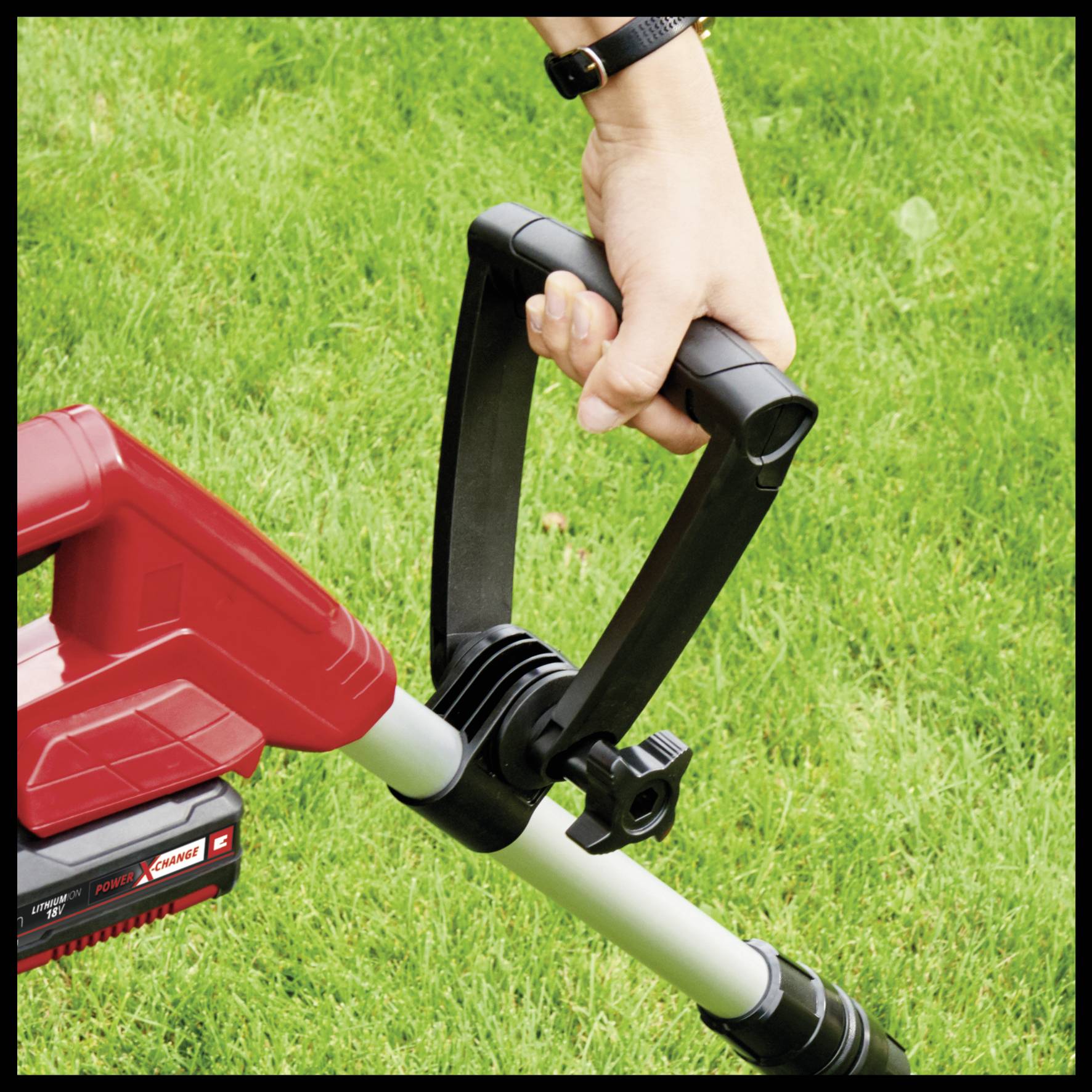 Eine Person hält einen roten Akku-Rasentrimmer über grünes Gras. Die Hand umgreift den Griff des Geräts, bereit zum Trimmen.