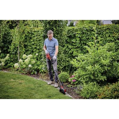 Ein Mann mäht mit einem elektrischen Rasentrimmer den Rasenrand in einem gepflegten Garten mit grünem Strauch- und Blumenbewuchs.