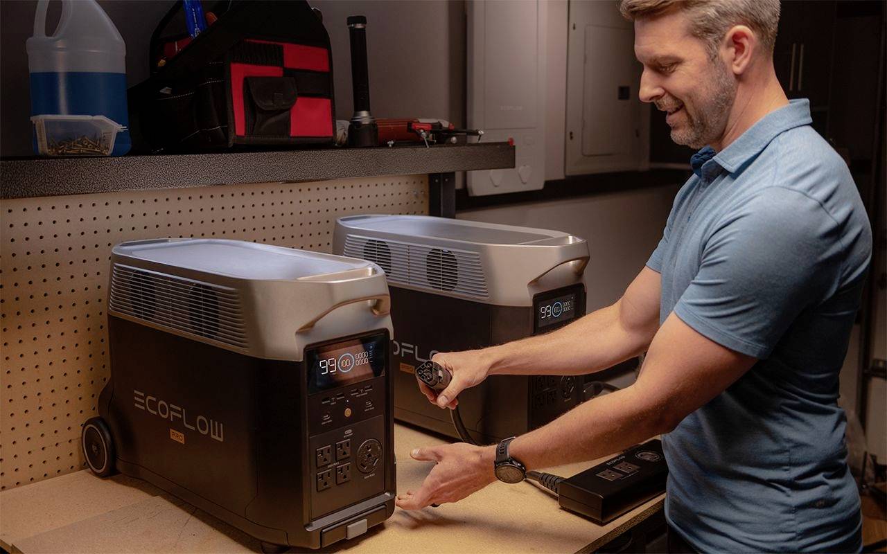 Ein Mann in einem blauen Shirt bedient zwei tragbare Stromgeneratoren in einer Werkstattumgebung.