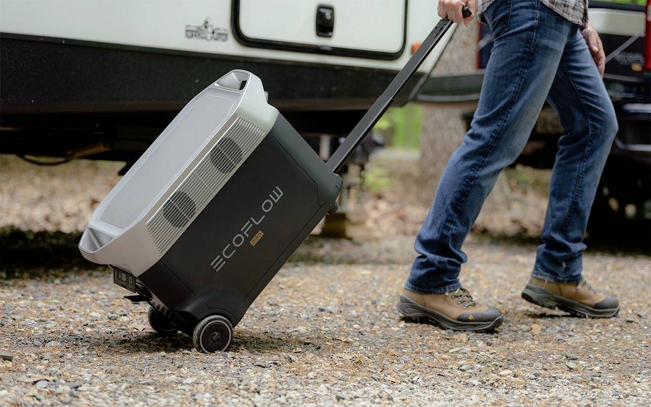 Eine Person zieht im Freien eine schwarze EcoFlow-Kühltasche auf Rädern. Sie trägt Jeans und Wanderschuhe.