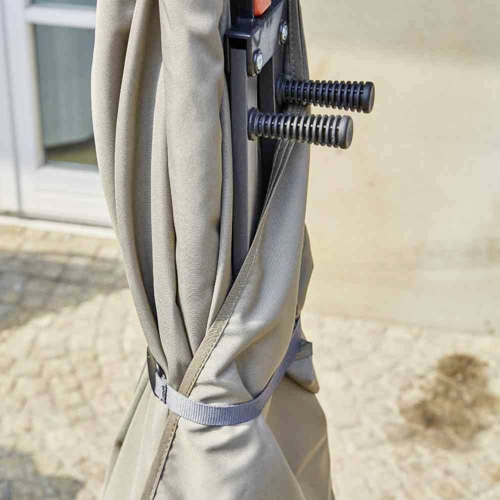 Ein zusammengeklappter Sonnenschirm steht auf einer Terrasse neben einem Gebäude. Der Schirm ist mit einem Band gesichert.