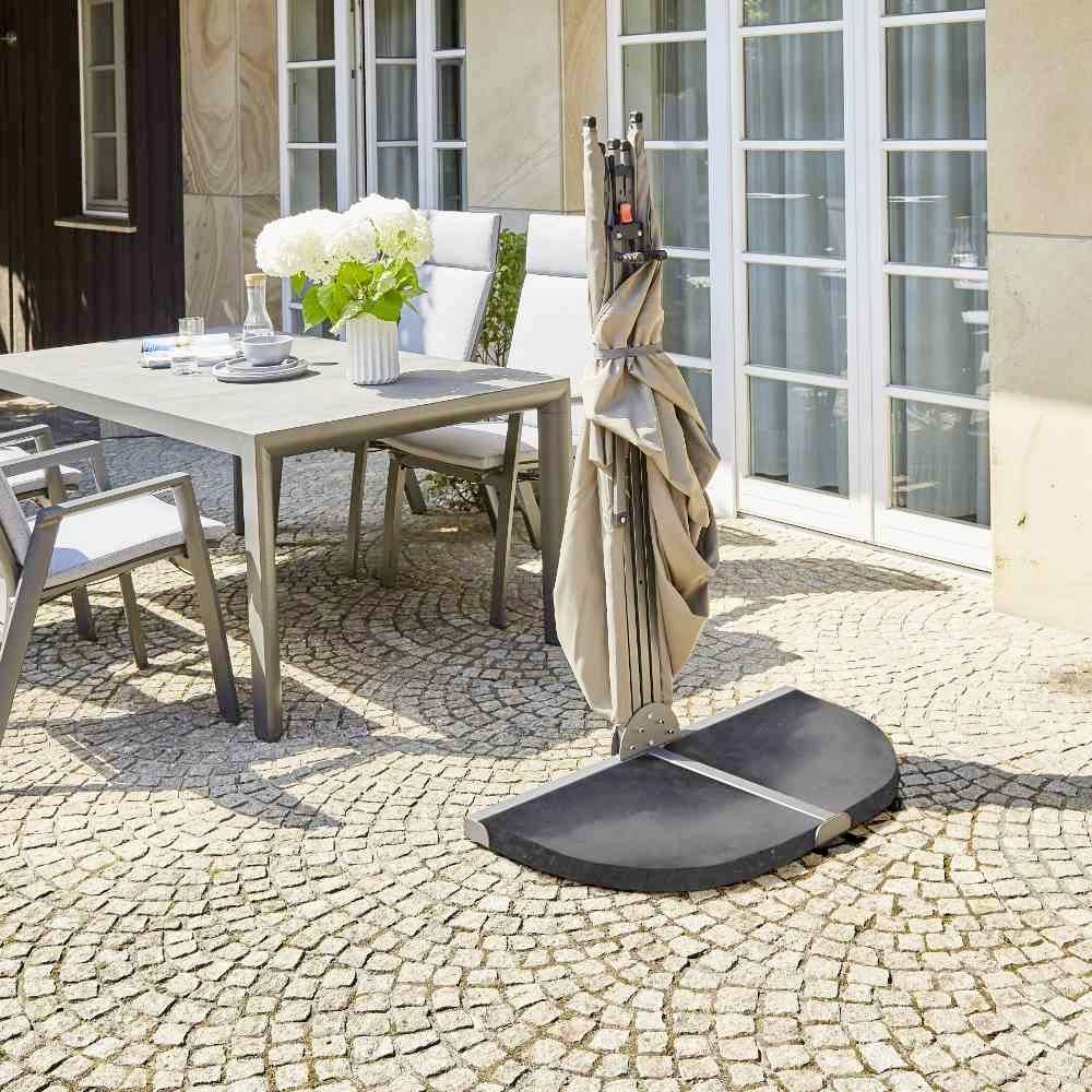 'Gartenmöbel-Set mit Tisch, vier Stühlen und Sonnenschirmständer auf gepflasterter Terrasse. Eine Vase mit weißen Blumen auf dem Tisch.'