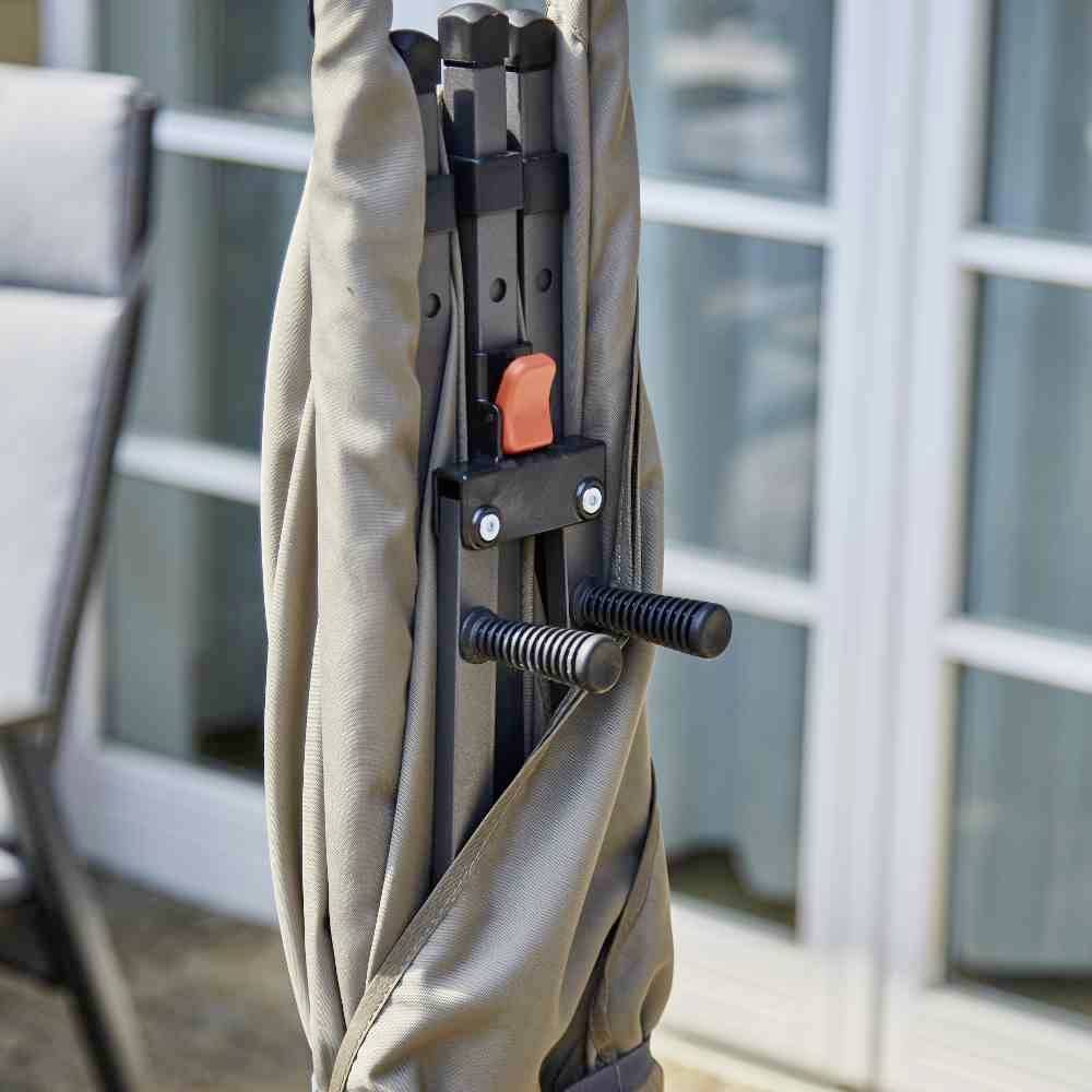 Ein geschlossener, beige Sonnenschirm in einem Gestell vor einer Glastür auf einer Terrasse.