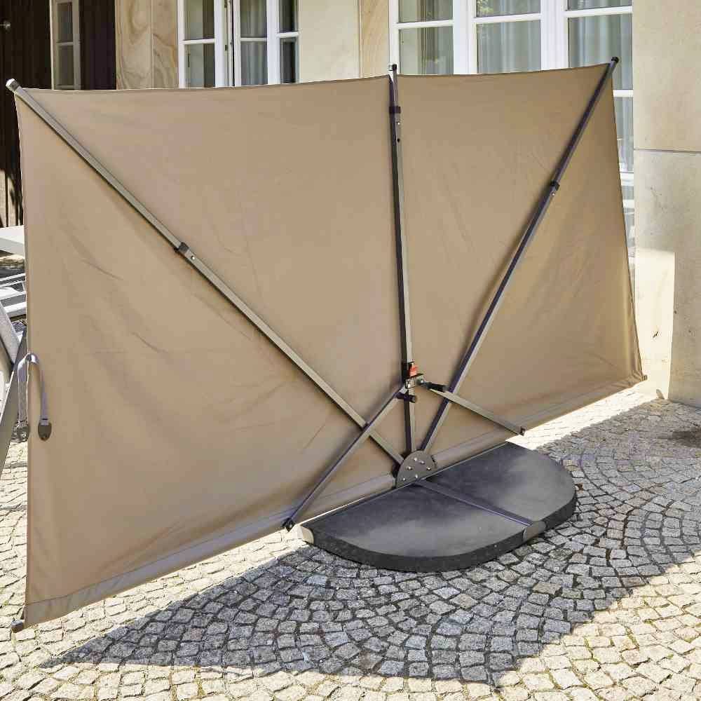 Brauner Windschutz auf einer Terrasse. Das Schutzelement hat einen stabilen Metallrahmen und steht auf einer gepflasterten Fläche.