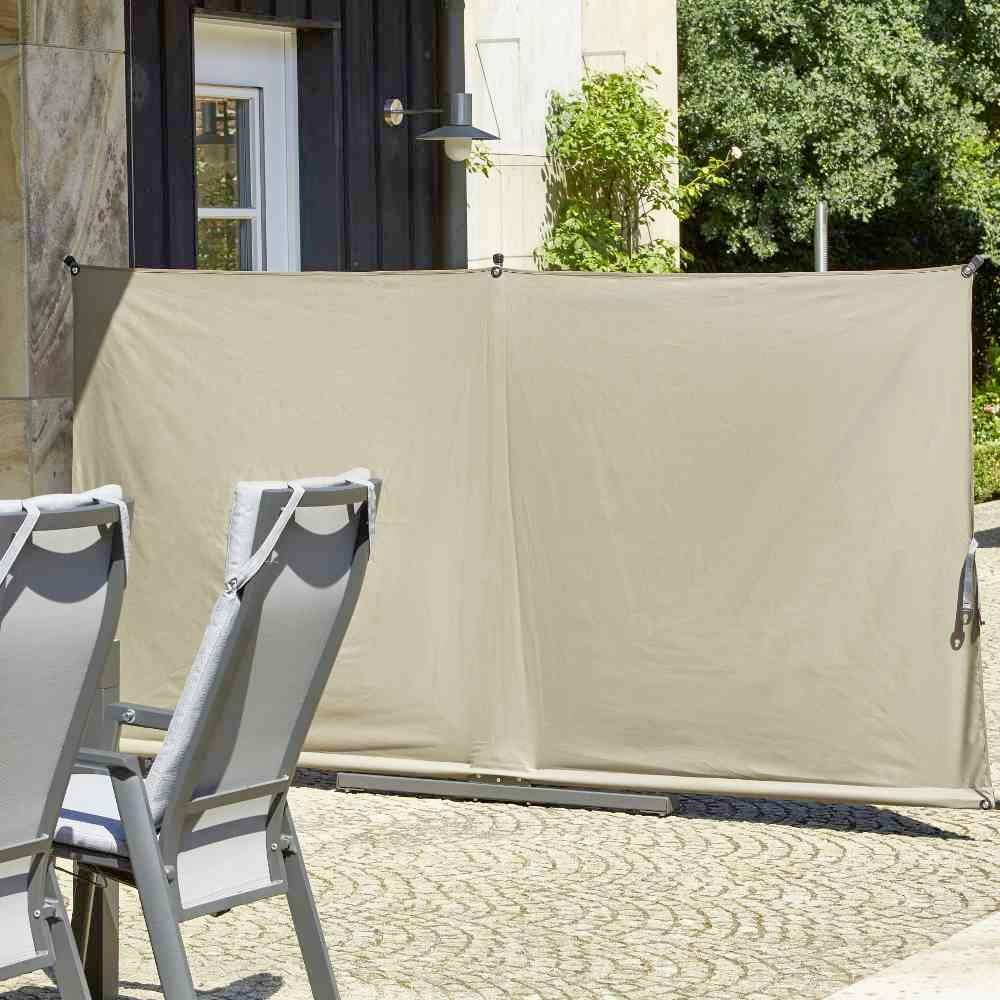 Ein grau-beiger Sichtschutz auf einer Terrasse bietet Privatsphäre, neben Gartenstühlen auf gepflastertem Boden bei Tageslicht.