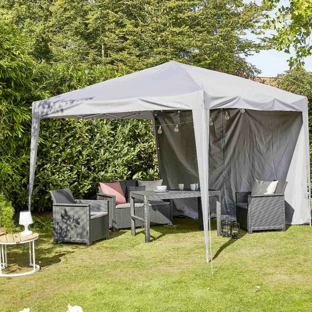 Ein graues Pavillonzelt steht im Garten, darunter stehen Rattanmöbel. Es ist umgeben von grünem Laub und bietet einen schattigen Sitzbereich.