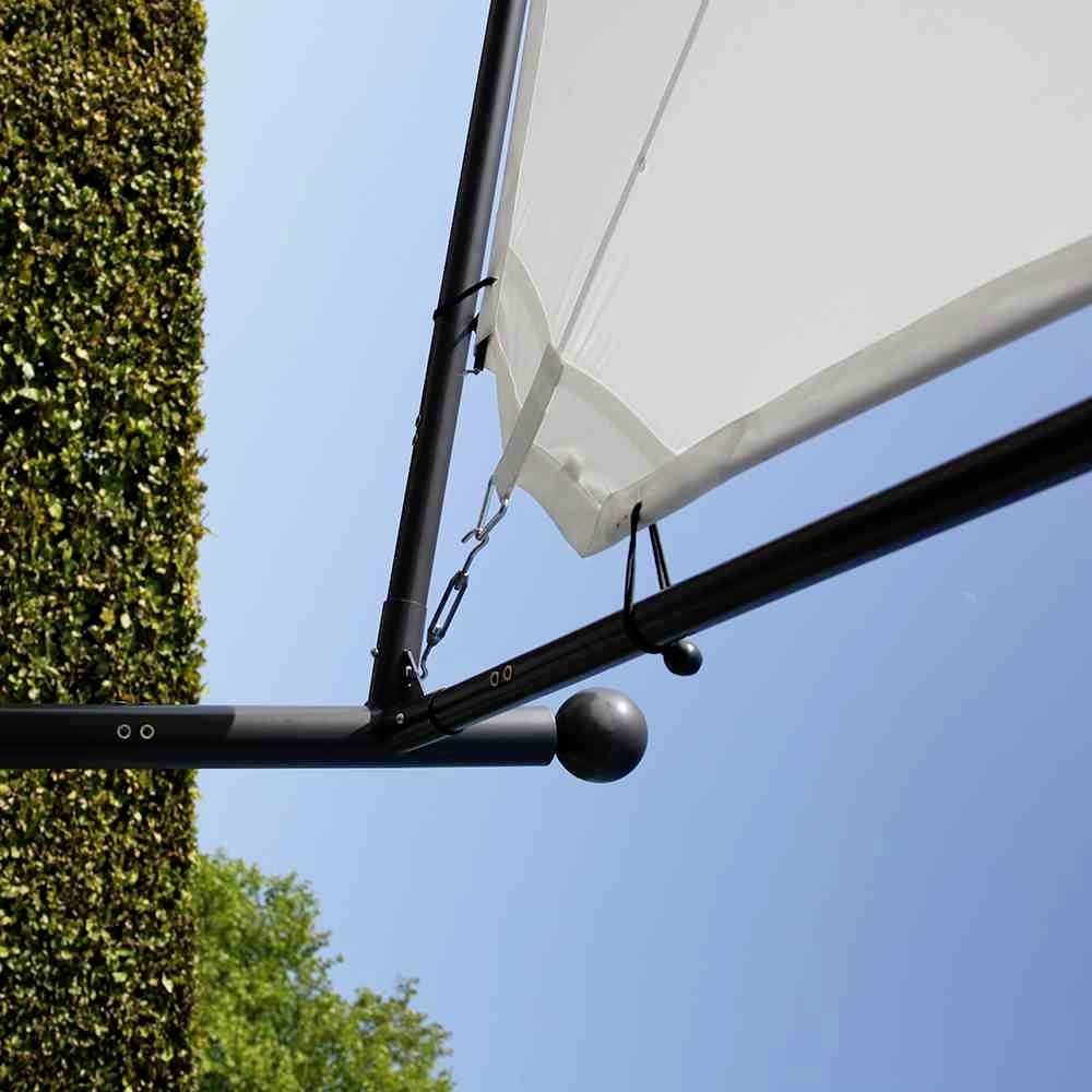 Ein Sonnensegel ist an einem Metallrahmen befestigt, der sich neben einer hohen Hecke befindet. Im Hintergrund ist blauer Himmel sichtbar.