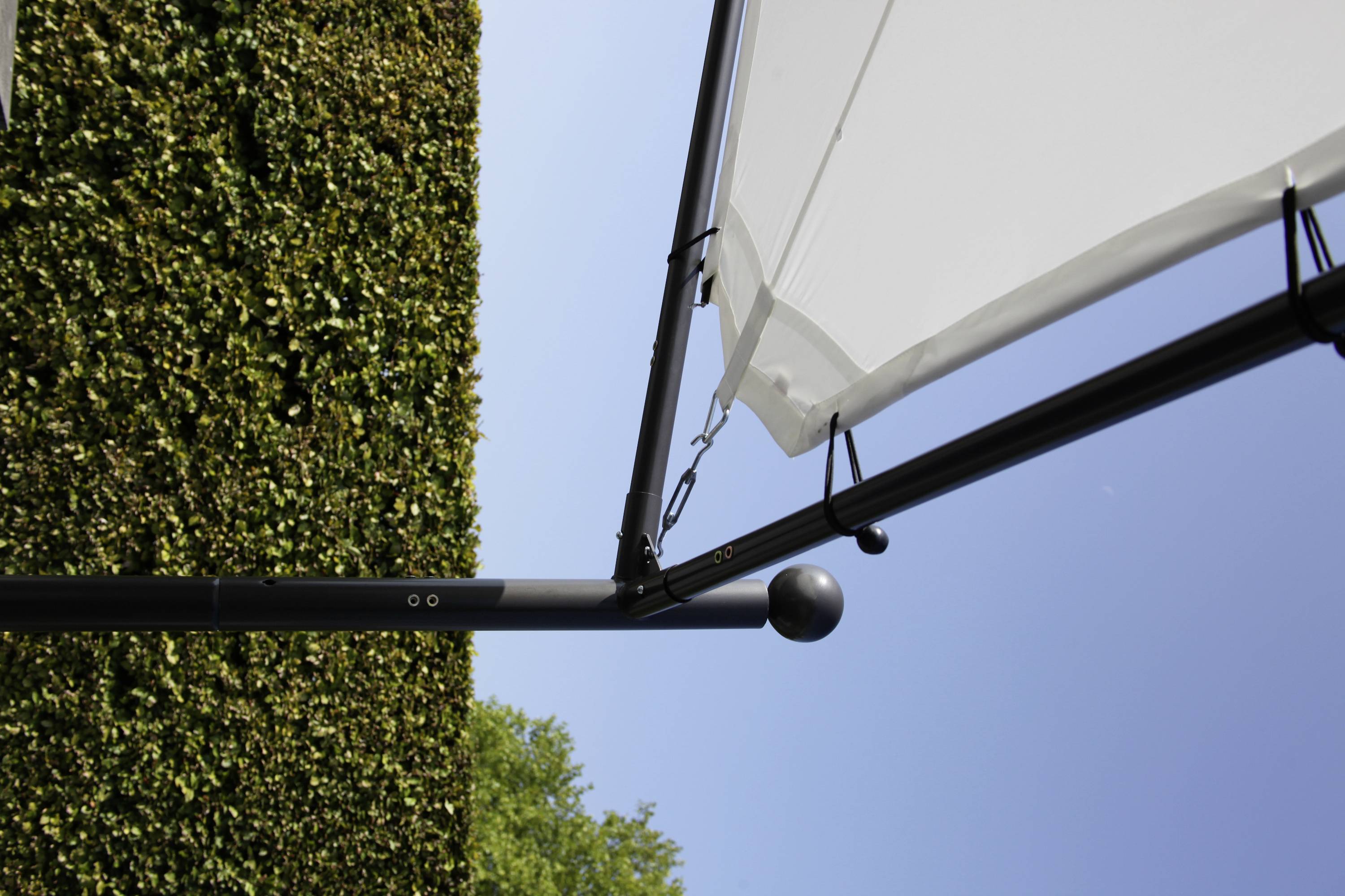 Blick nach oben auf einen offenen Sonnenschirm mit schwarzem Gestänge vor einem klaren blauen Himmel und einer hohen Hecke.