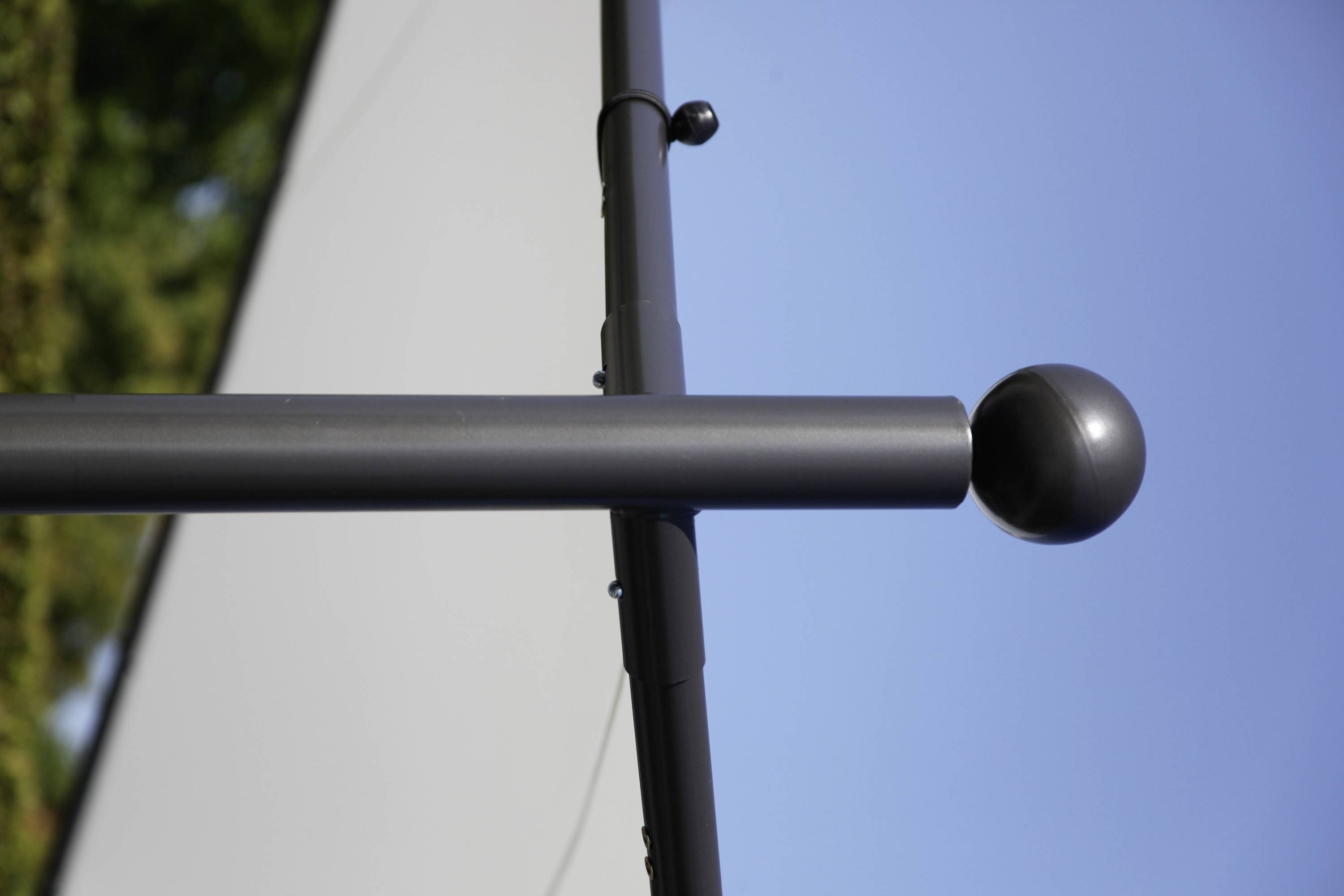 Ein graues Metallgestänge mit einem runden Ende vor einem blauen Himmel, möglicherweise Teil einer Fahnenstange oder Zeltrahmen.