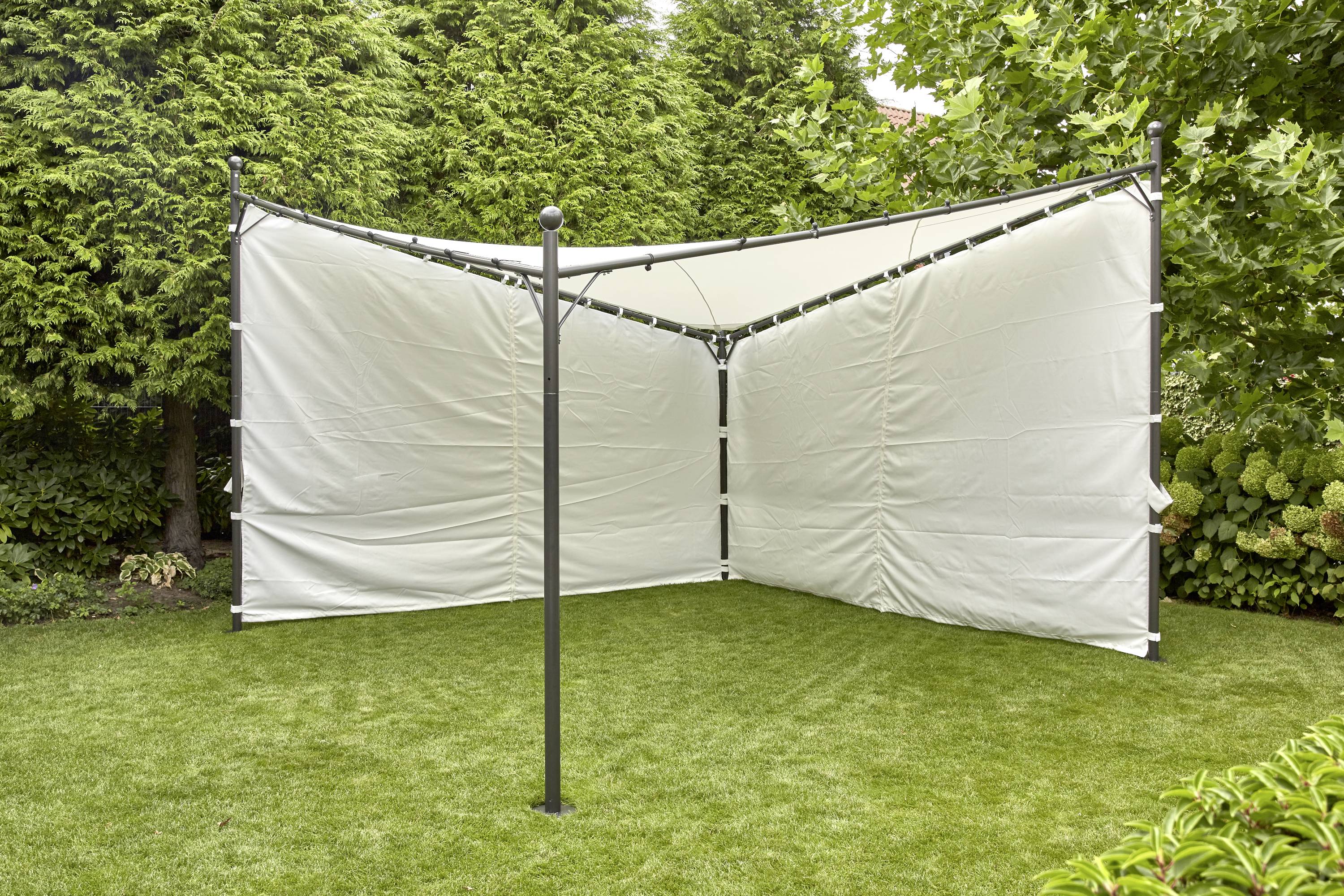 Ein Pavillon mit weißen Planen steht in einer Ecke eines gepflegten Gartens auf einer grünen Rasenfläche, von hohen Bäumen umgeben.