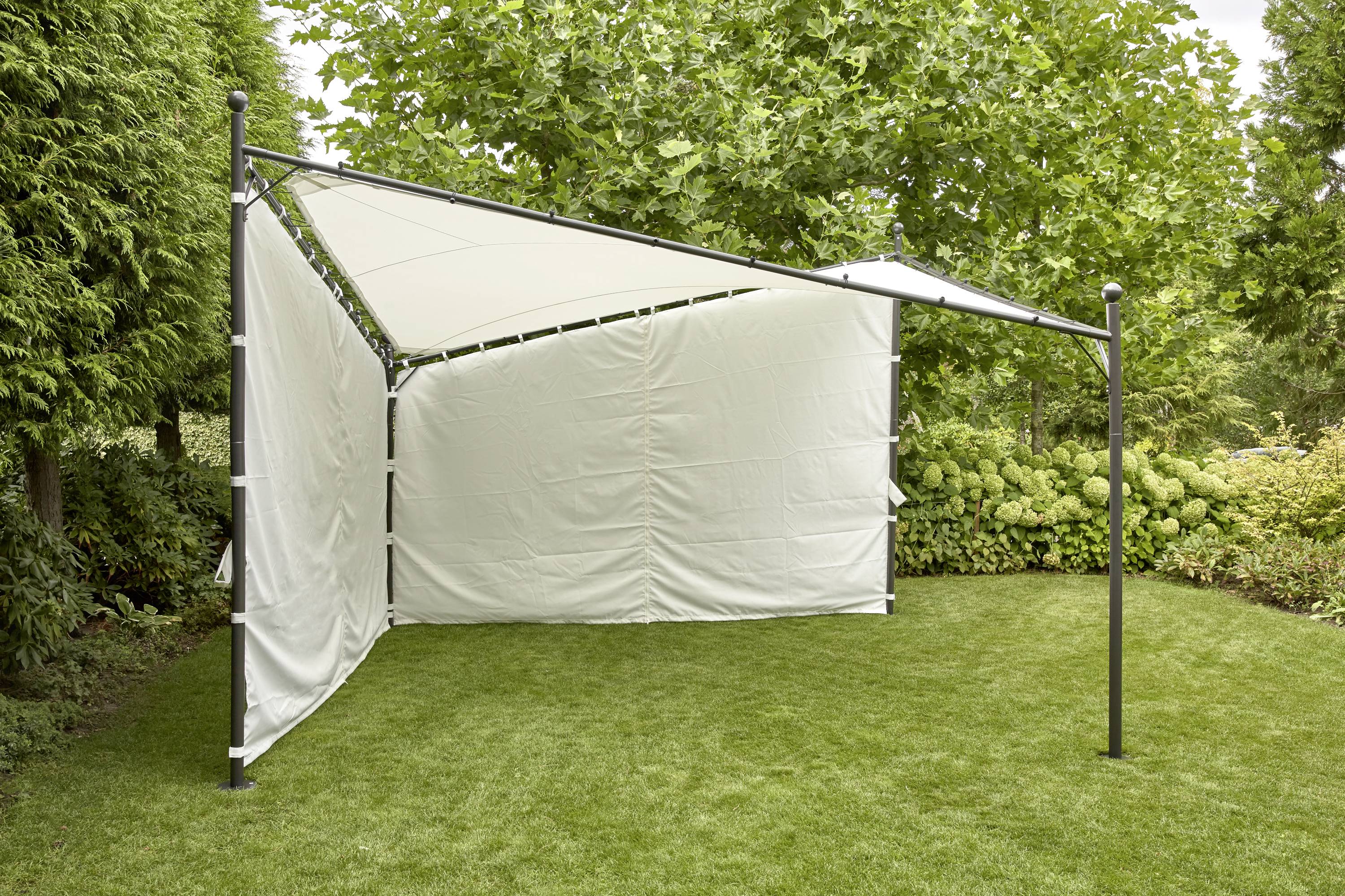 Ein weißes Sonnensegel auf einer Wiese, umgeben von üppigem Grün und Büschen, bietet Schatten und Schutz vor der Sonne.