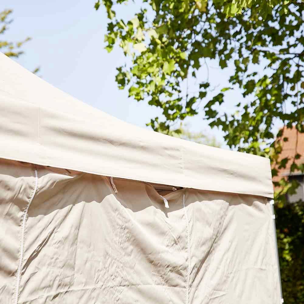 Ein beiger Pavillon unter Bäumen in einem sonnigen Garten.