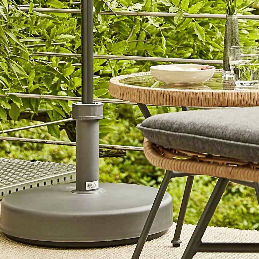 Ein gemütlicher Terrassenbereich mit einem runden Tisch, auf dem ein Getränk und ein Teller stehen, umgeben von grüner Vegetation.