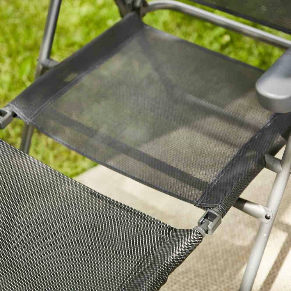 Ein Klappstuhl steht auf einer Rasenfläche. Die Sitzfläche und Rückenlehne sind aus schwarzem Netzmaterial.