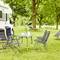 Wohnmobil auf einer Wiese mit Campingstühlen und Tisch im Vordergrund; im Hintergrund Bäume und Hängematte, Sommeratmosphäre.