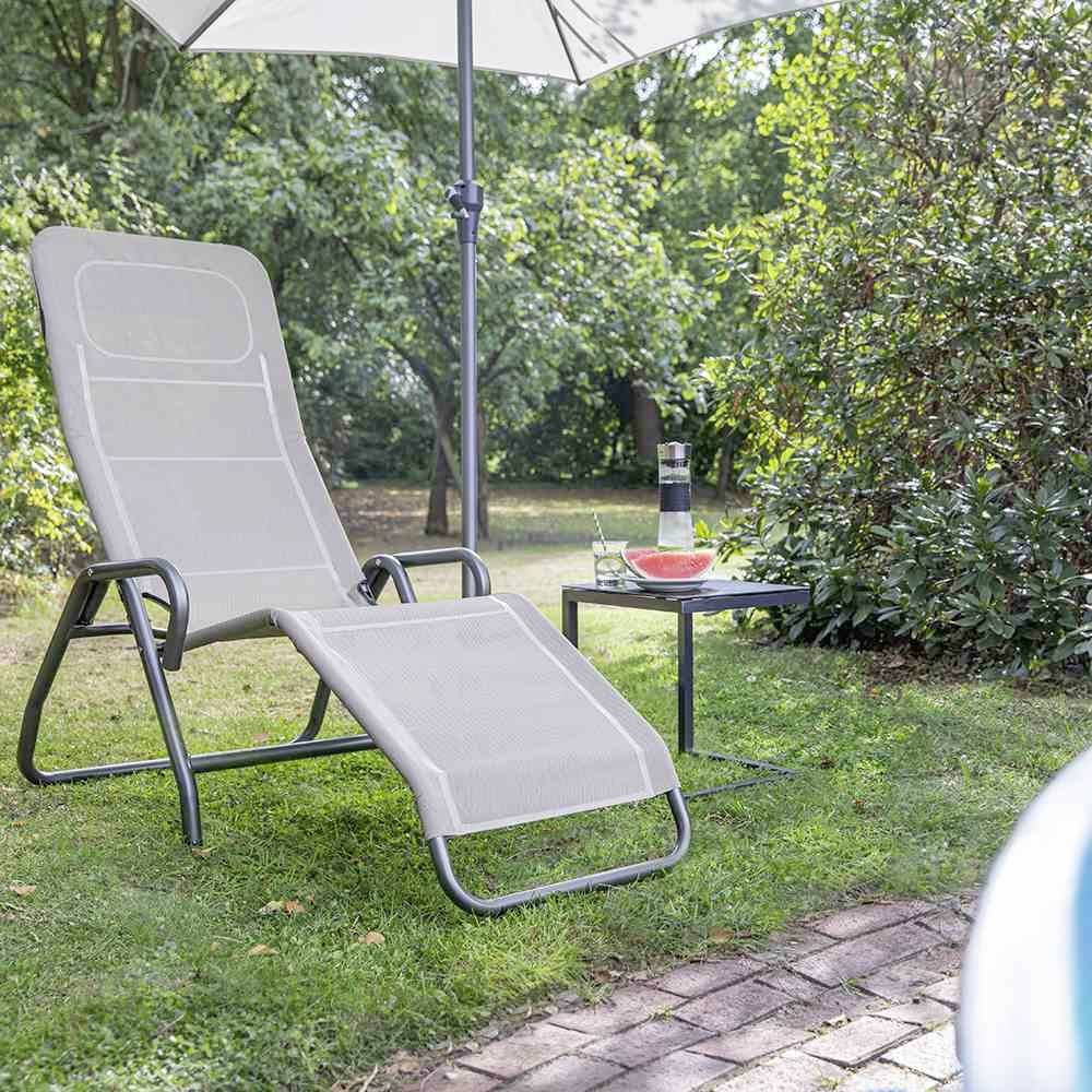 'Ein grauer Gartenstuhl mit passender Fußstütze steht unter einem weißen Sonnenschirm, daneben ein kleiner Tisch mit Karaffe und Schale.'