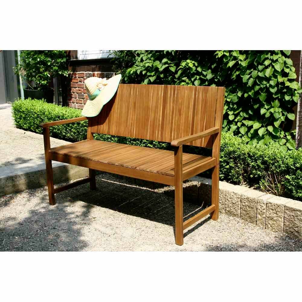 Holzbank mit Armlehnen steht in einem Garten auf einem Kiesweg, umgeben von grünen Sträuchern; Sonnenhut liegt auf der Lehne.