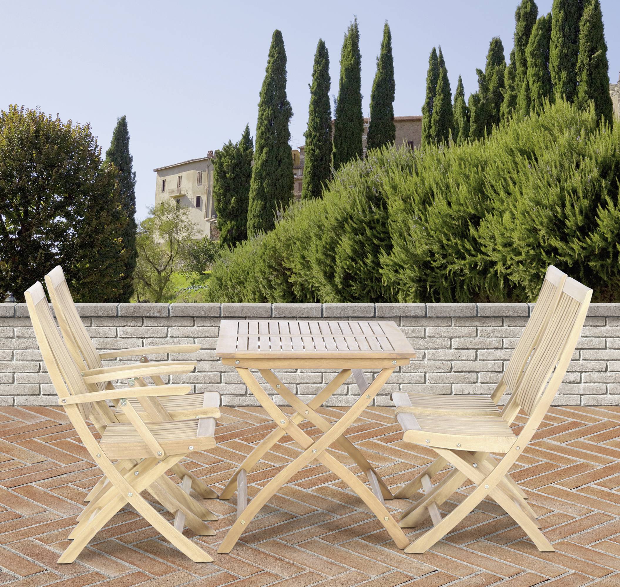 Holzterrassentisch mit vier Klappstühlen auf einem Ziegelsteinboden, umgeben von hohen Bäumen und einem mediterranen Gebäude im Hintergrund.