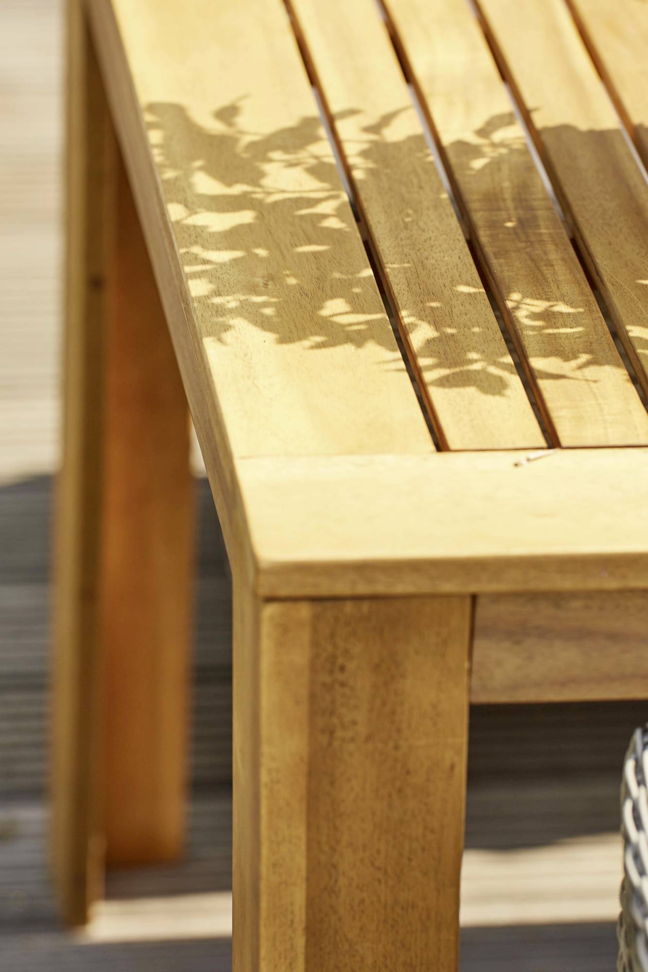 Ein hölzerner Tisch mit Sonnenschatten von Pflanzen auf der Oberfläche, auf einer Terrasse bei Tageslicht.