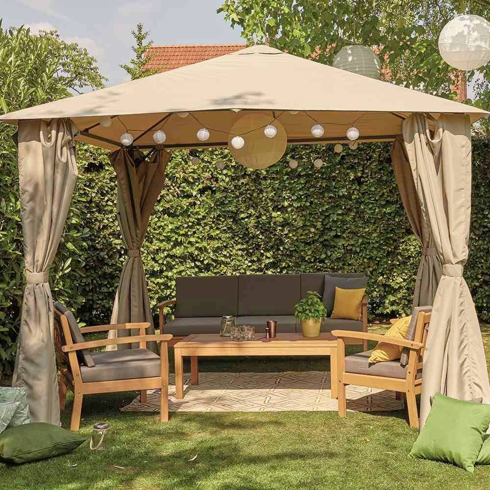 Ein Gartenpavillon mit Vorhängen, zwei Holzbänken und einem Tisch darunter. Es gibt Lichterketten und Kissen. Im Hintergrund Hecke.