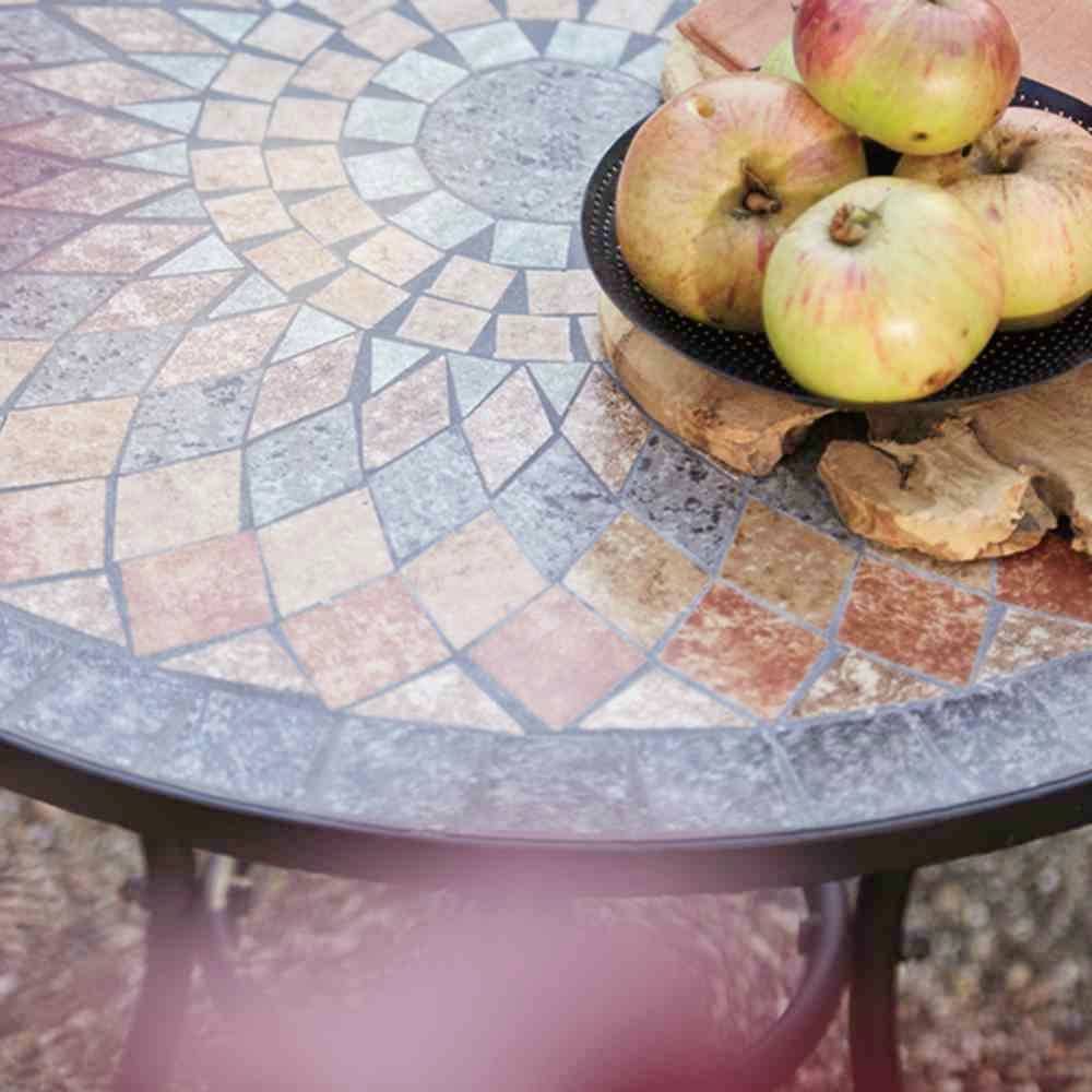 Fünf rote Äpfel liegen auf einem runden Tisch mit Mosaikfliesenmuster im Freien. Der Tisch hat eine dekorative Steinoberfläche.