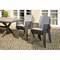 Gartenmöbel-Set mit rechteckigem Holztisch und sechs gestapelten, grauen Stühlen, auf einer gepflasterten Terrasse vor Fenstern.