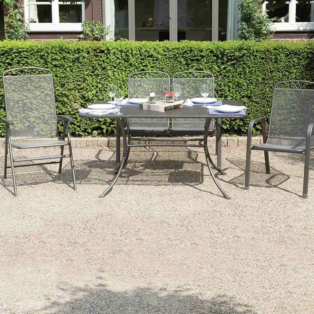 Ein Garten mit zwei Stühlen und einem Tisch, gedeckt für zwei Personen, umgeben von grünen Büschen vor einem Gebäude.
