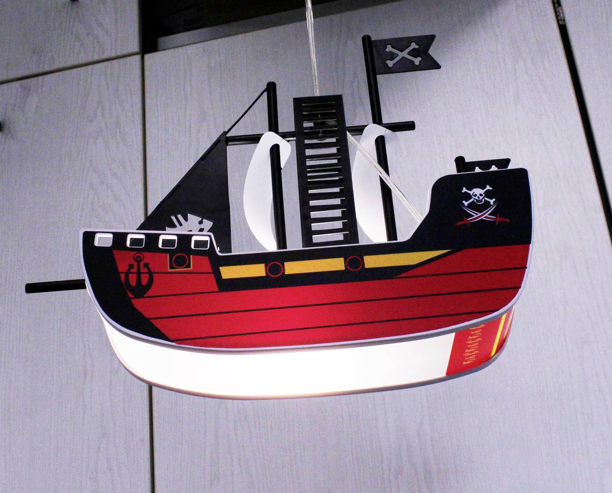Eine Piratenschiff-Deckenlampe mit rotem Rumpf und Totenkopf-Flagge hängt von der Decke.