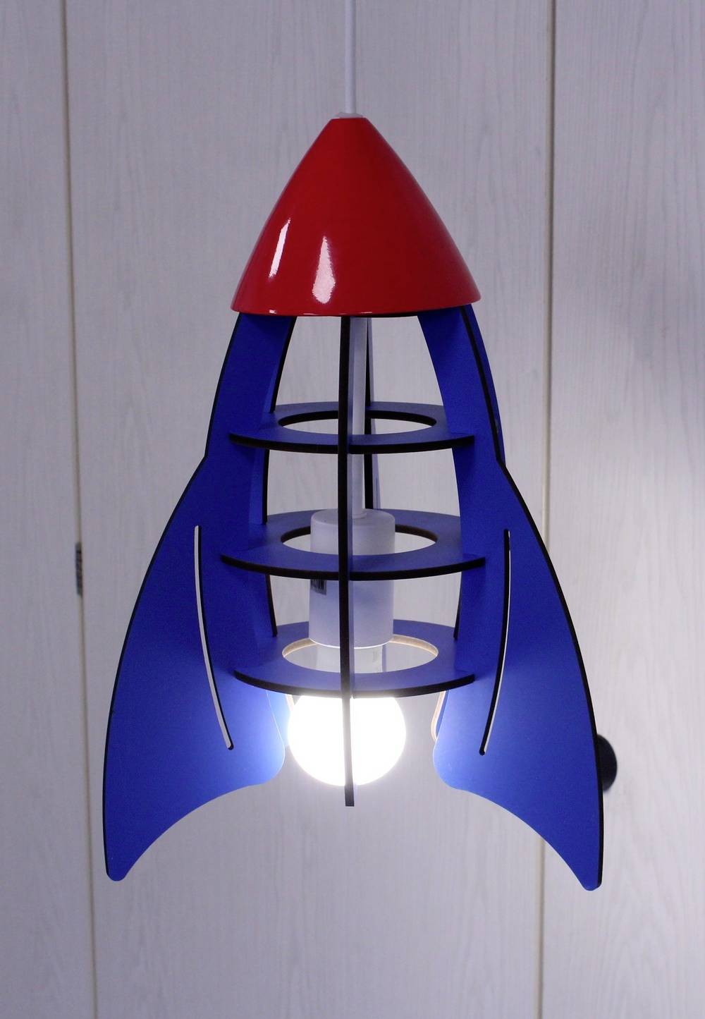 Eine Hängelampe in Form einer Rakete, blau mit roter Spitze, beleuchtet einen Raum.