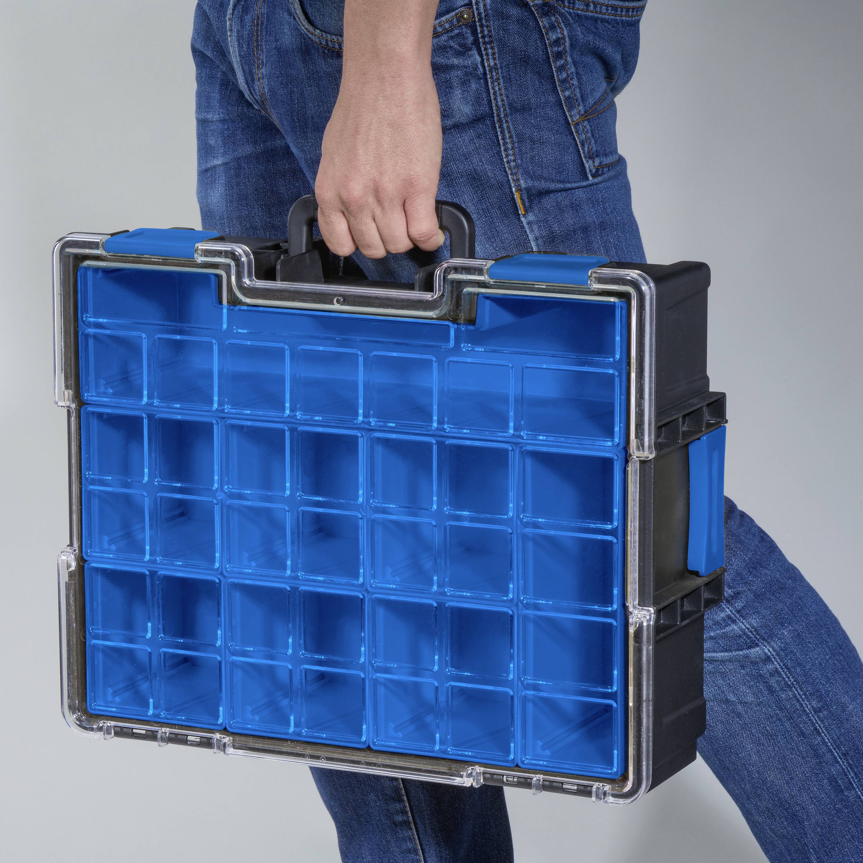 Eine Person trägt einen Kunststoff-Werkzeugkoffer mit vielen kleinen, leeren Fächern, geeignet zur Aufbewahrung und Organisation von Kleinteilen.