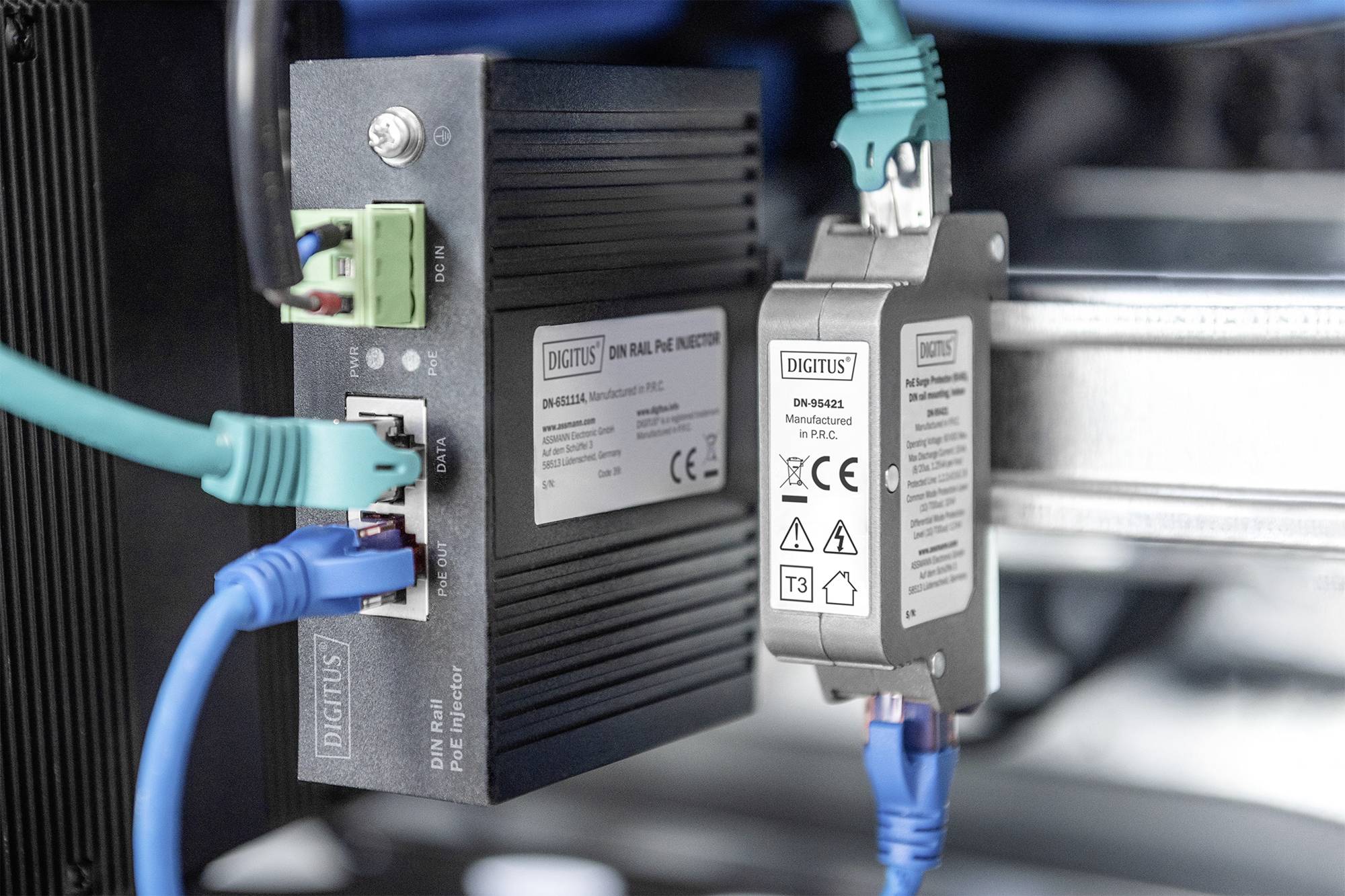 Ein schwarzer Netzwerkadapter und ein Überspannungsschutz sind mit Netzwerkkabeln verbunden. Beide Geräte sind mit CE-Zertifikaten gekennzeichnet.