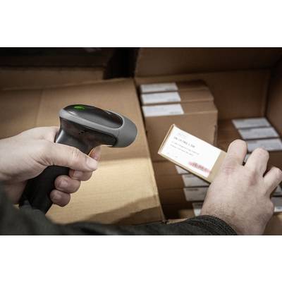 Eine Person verwendet einen Barcodescanner, um ein Etikett auf einem Karton zu scannen. Im Hintergrund sind weitere Kartons sichtbar.