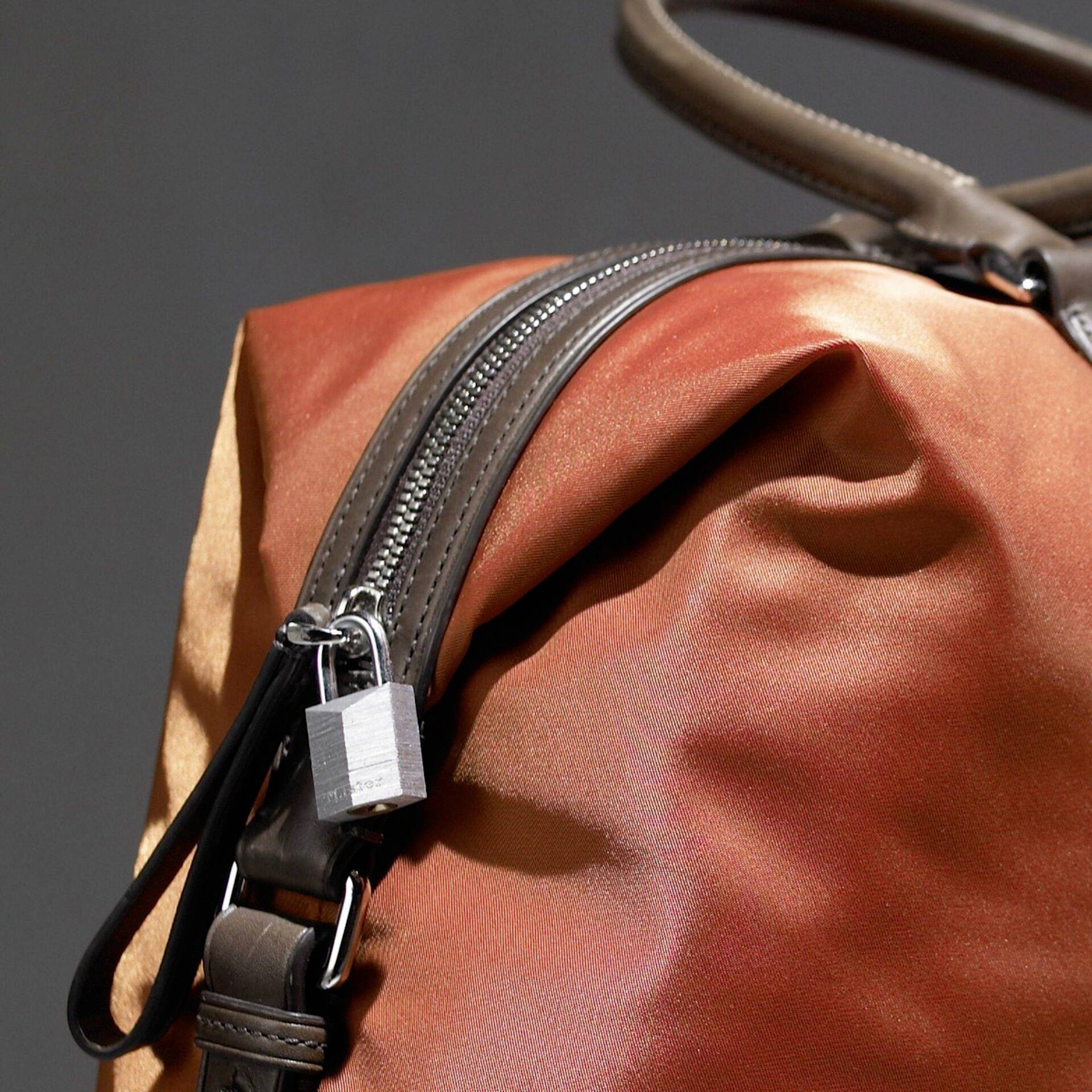 Eine orange Lederhandtasche mit silbernem Reißverschluss und schwarzem Trageriemen, Nahaufnahme des Designs.