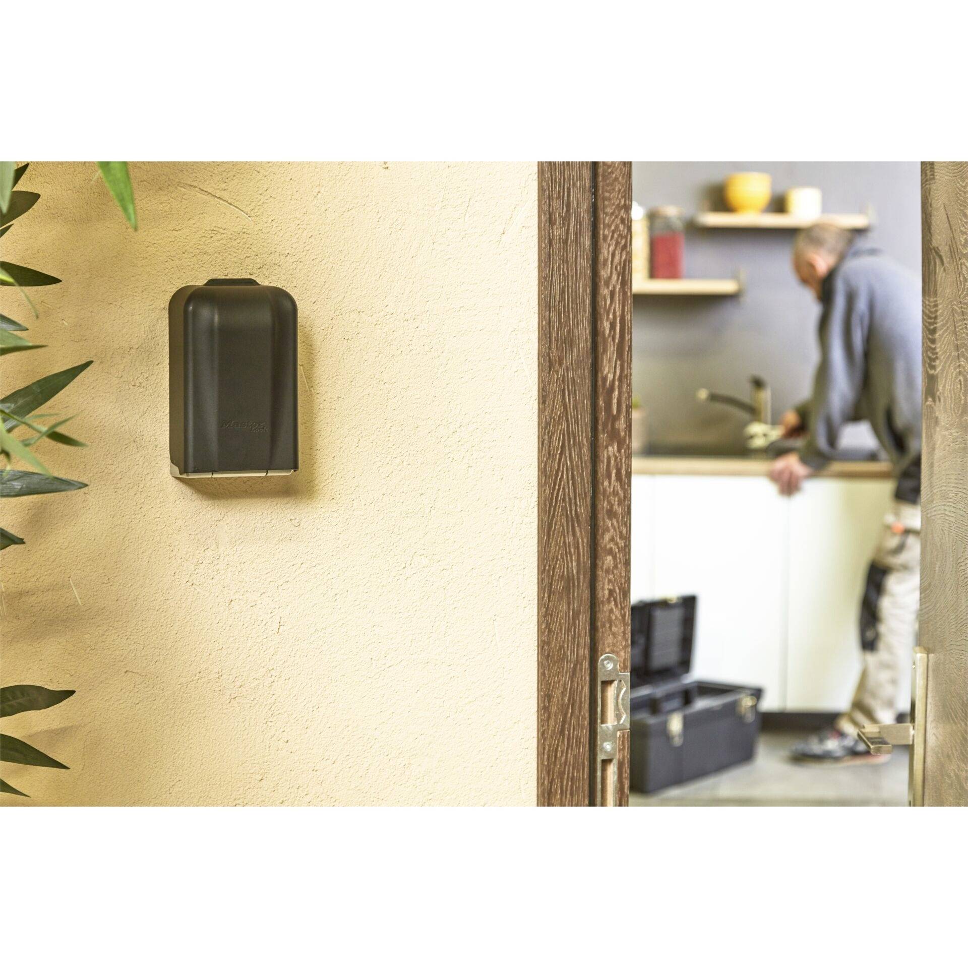 Ein Handwerker steht in einer Küche und arbeitet an einem Waschbecken. Im Vordergrund befindet sich ein dunkler Kasten an der Wand.