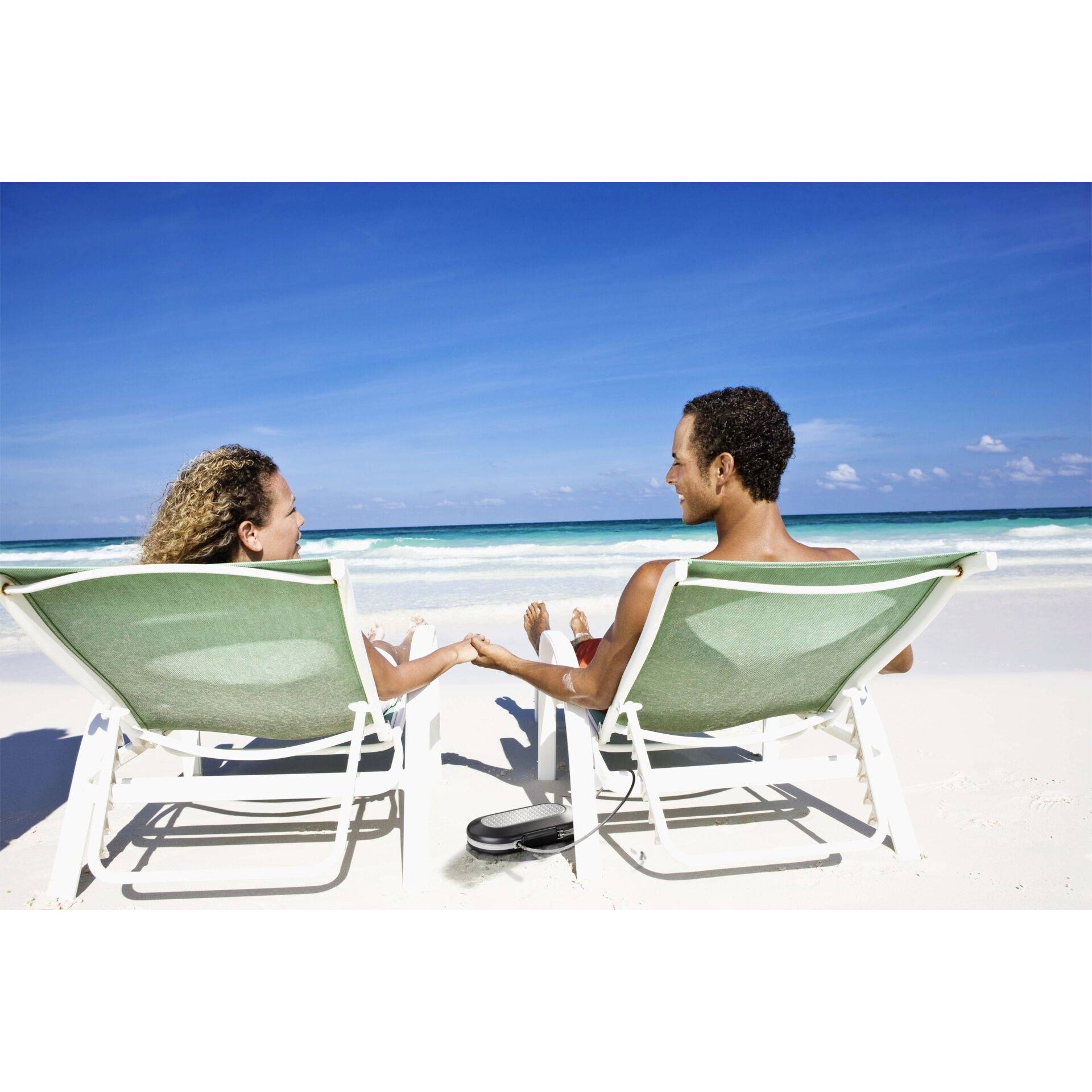 Ein Paar sitzt entspannt auf Liegestühlen am Strand, hält Händchen und schaut auf das Meer an einem sonnigen Tag.