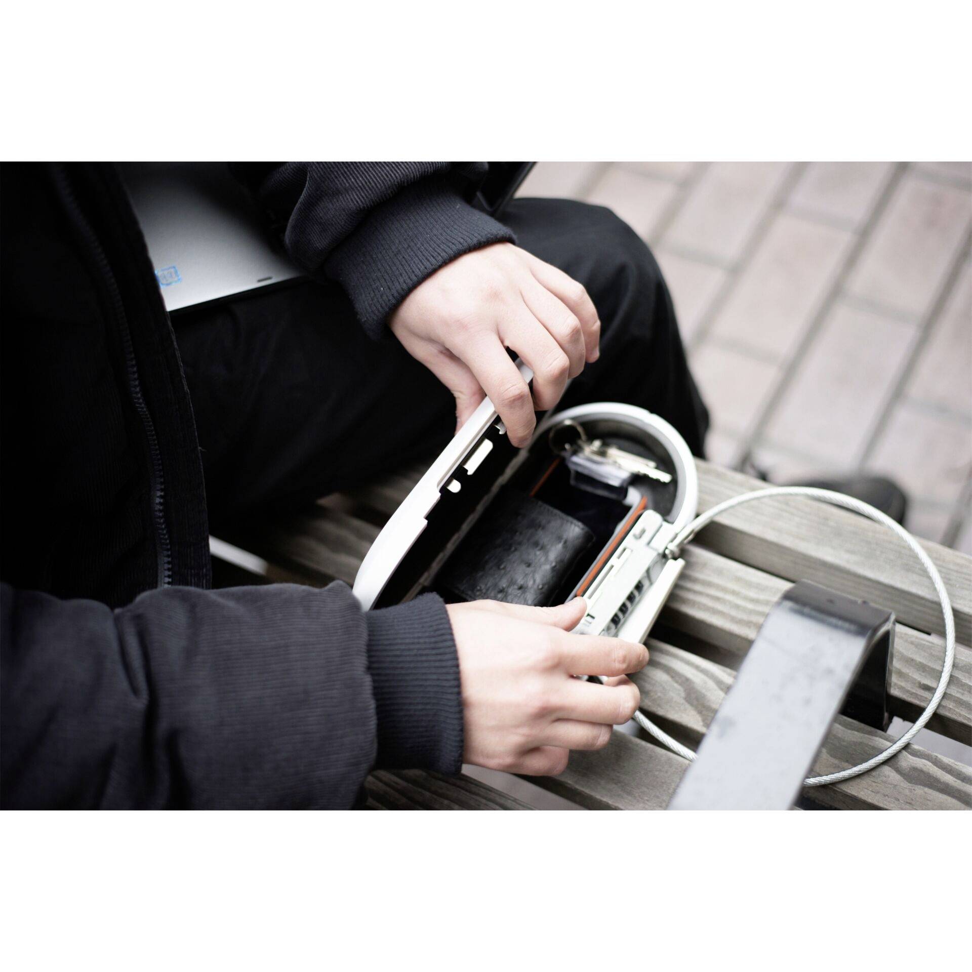 Eine Person sitzt auf einer Bank und hält ein offenes Schloss mit einem Kabel.