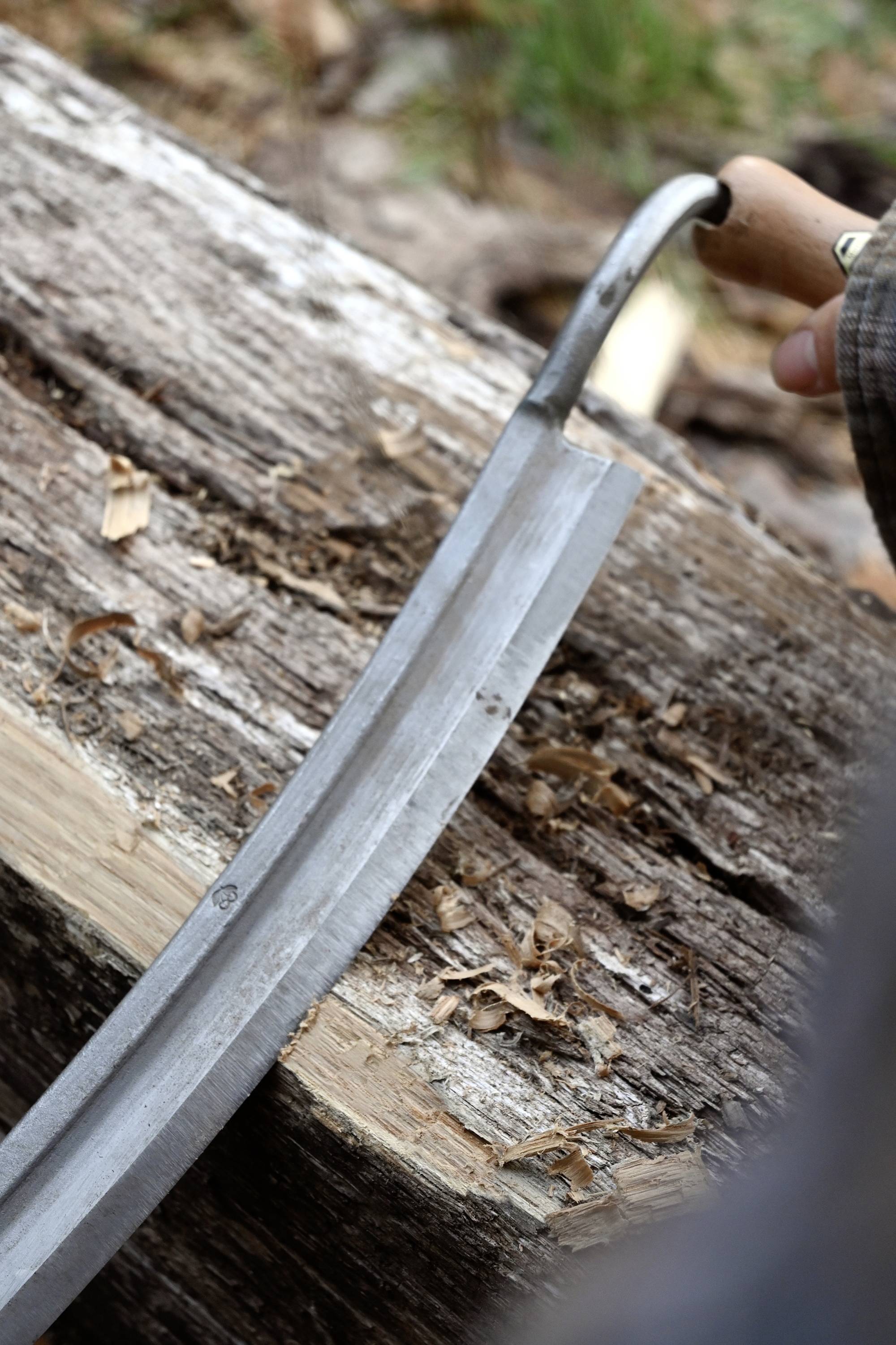 Eine Hand zieht einen breiten Hobel über ein Stück Holz, um es zu glätten. Holzspäne sind sichtbar auf der Oberfläche.