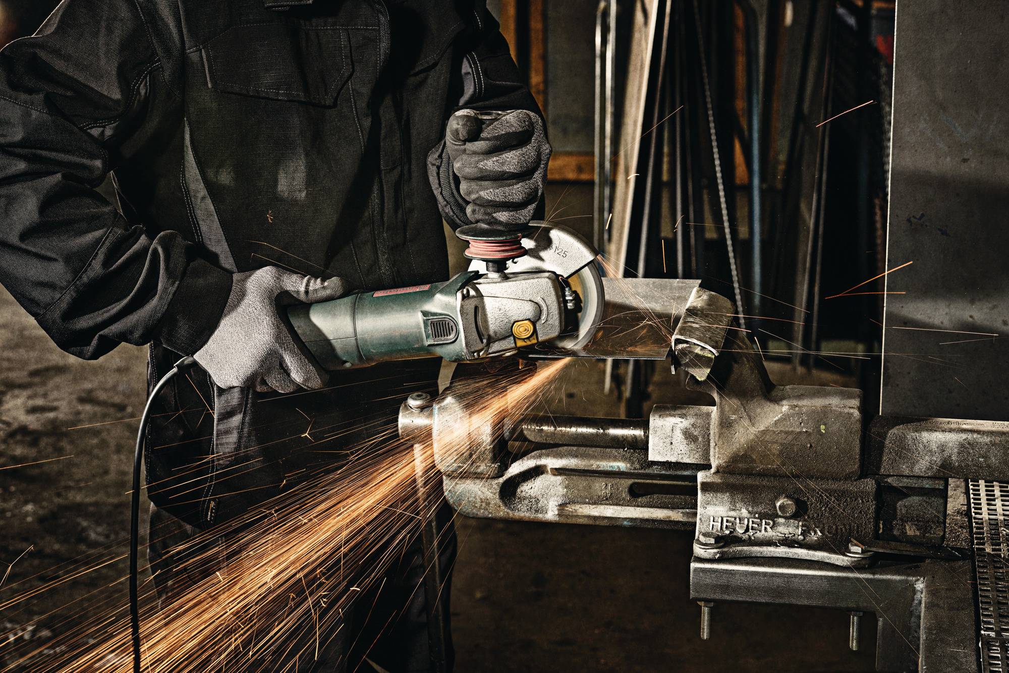 Arbeiter, der in einer Werkstatt ein Winkelschleiffer zum Zuschneiden von Metall verwendet, wobei Funken von der Schleifscheibe fliegen.