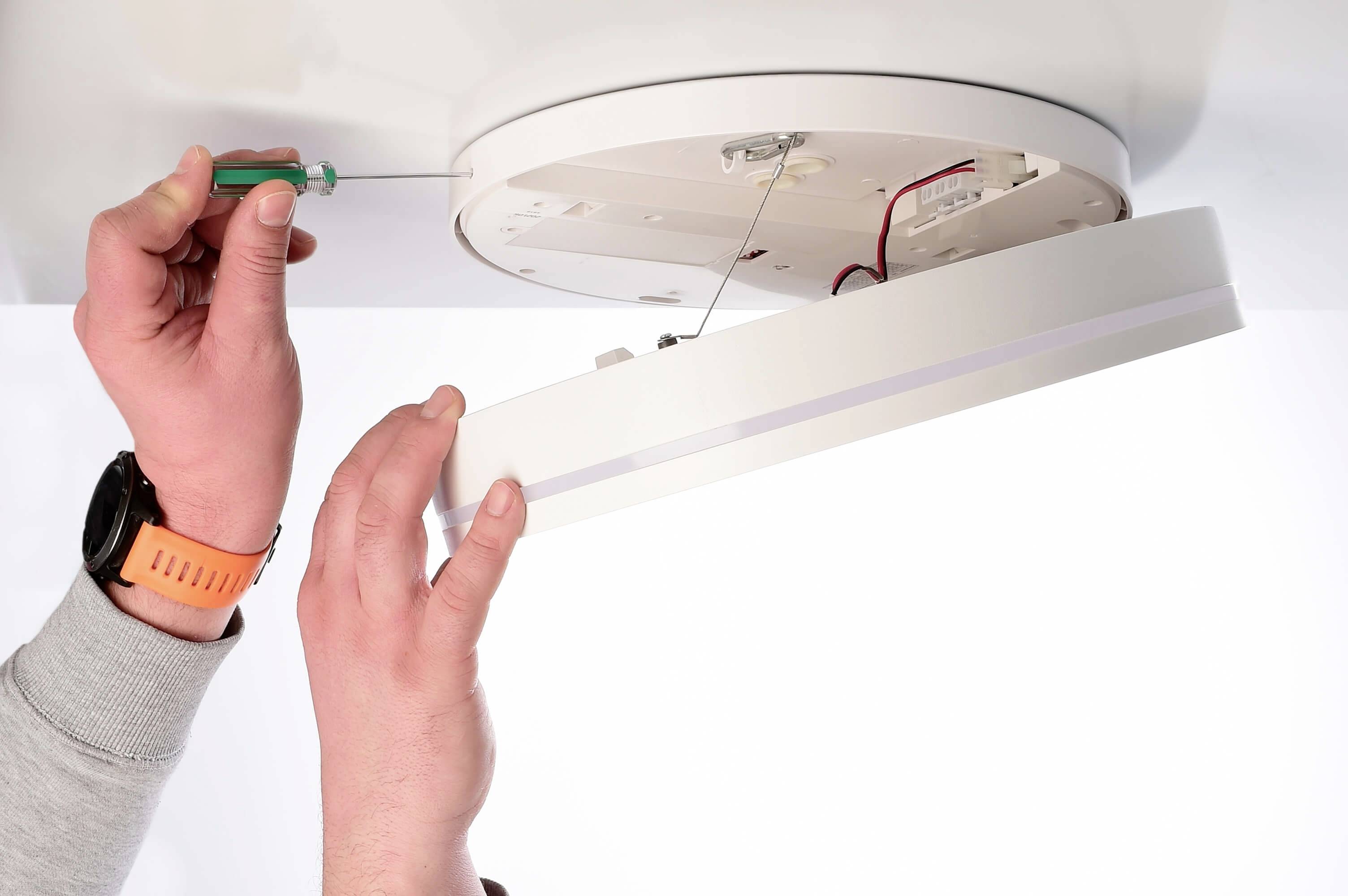 Eine Person installiert eine runde Deckenlampe mit einem Schraubenzieher. Die Lampe ist offen und zeigt interne Verkabelung.