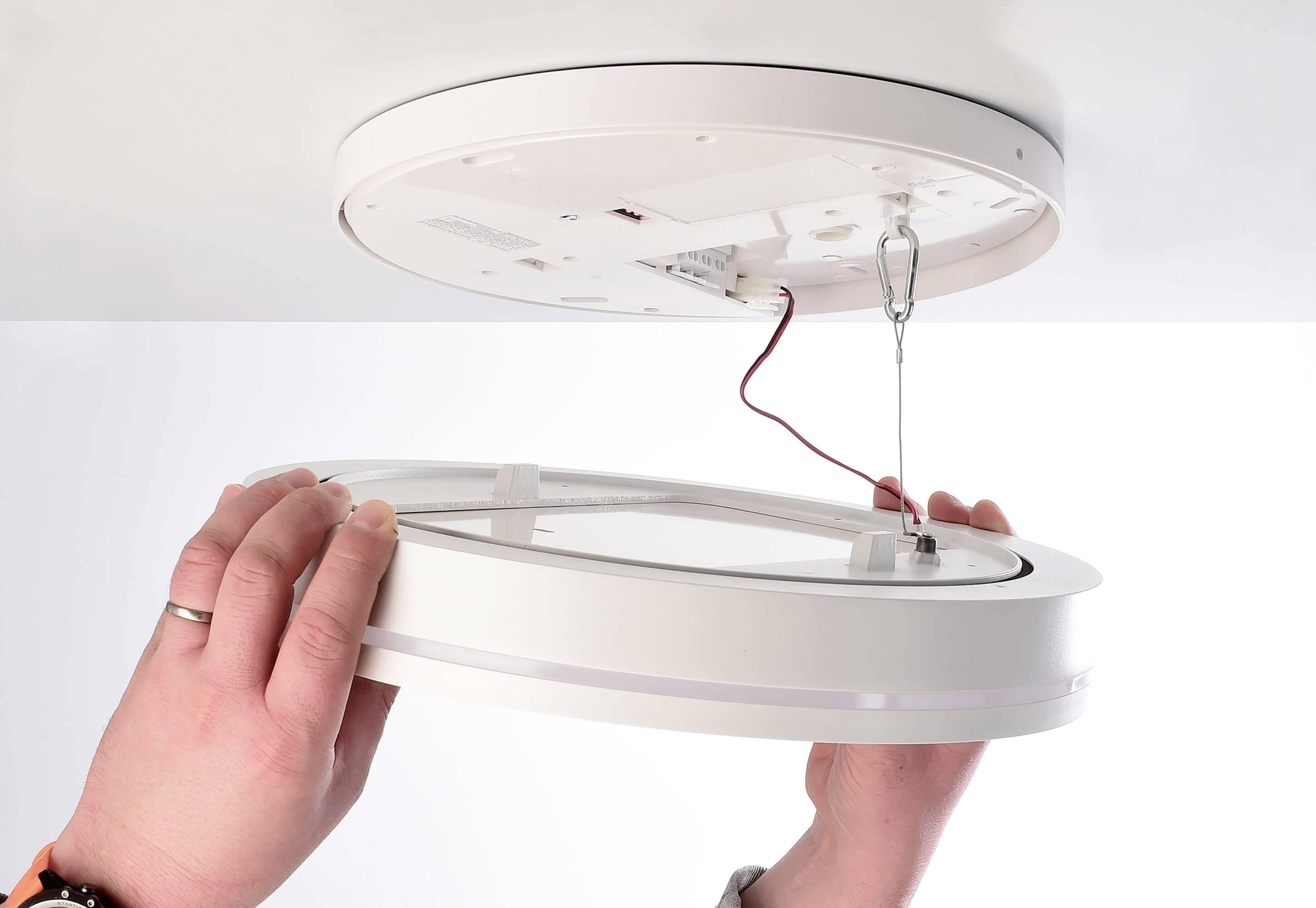 Zwei Hände montieren eine runde LED-Deckenleuchte mit Kabelverbindung.